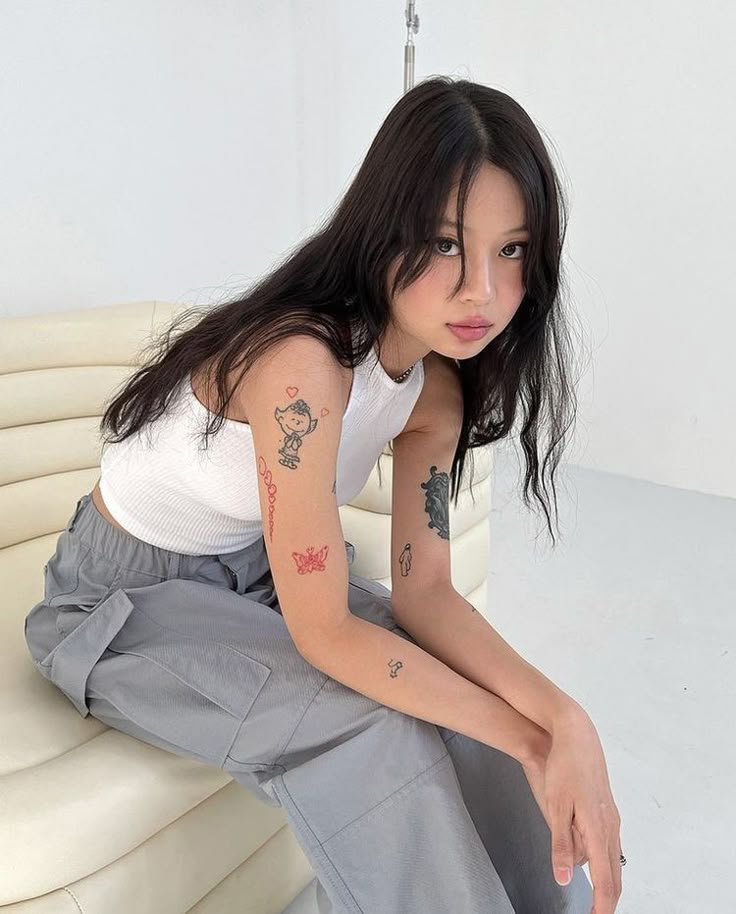 a woman sitting on top of a white couch next to a wall with tattoos on her arm