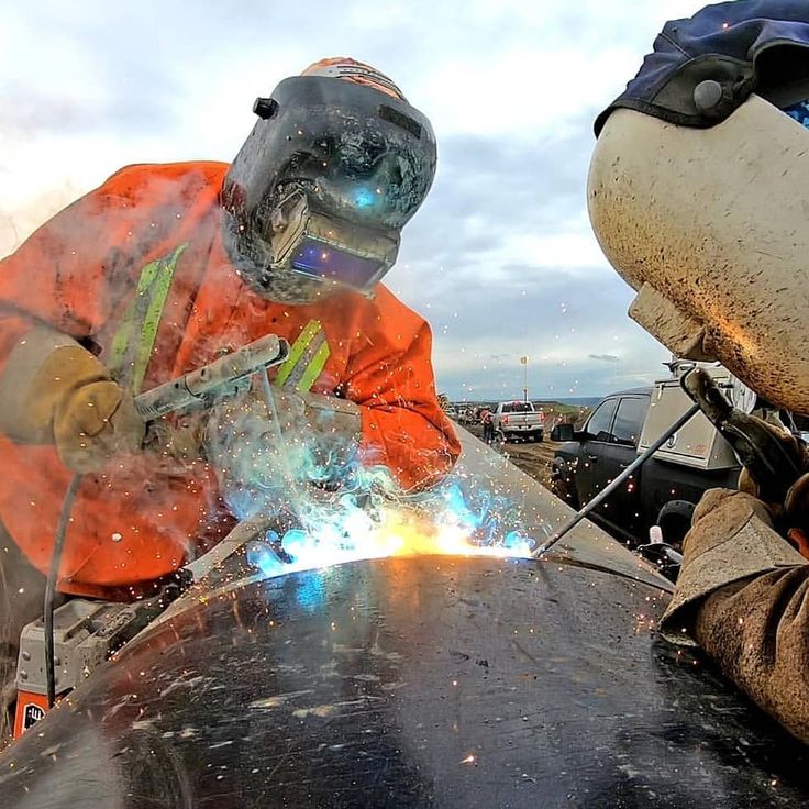 welder in an orange safety jacket grinding metal with a grinder on the table