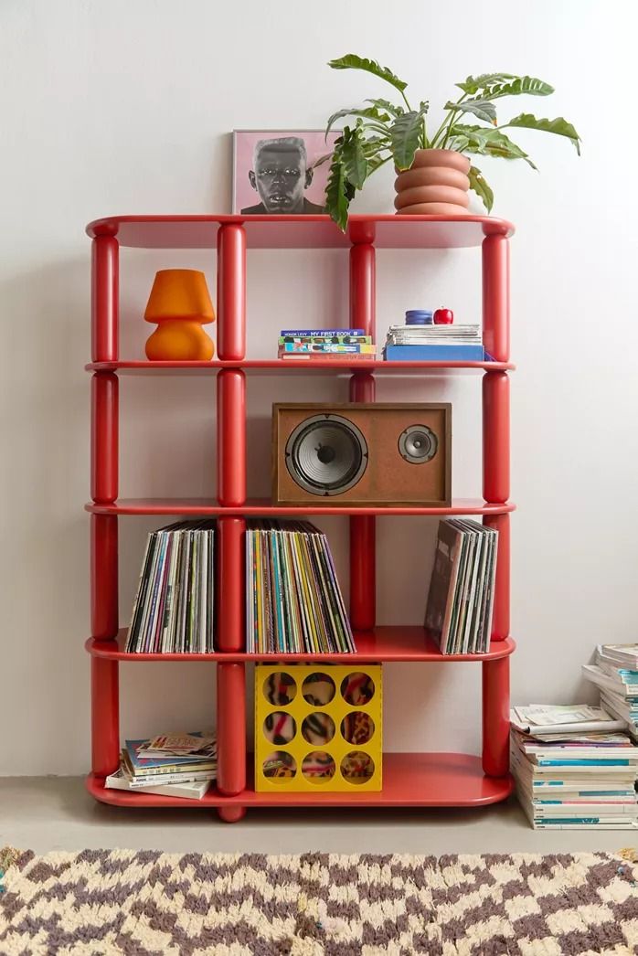 a red shelving unit with record players and various records on it in front of a white wall