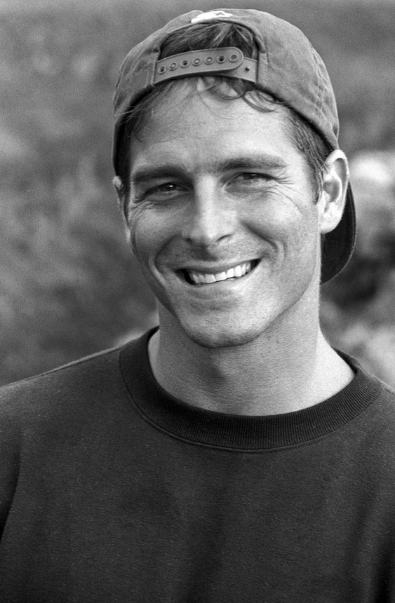 a black and white photo of a man wearing a hat smiling at the camera with his eyes closed