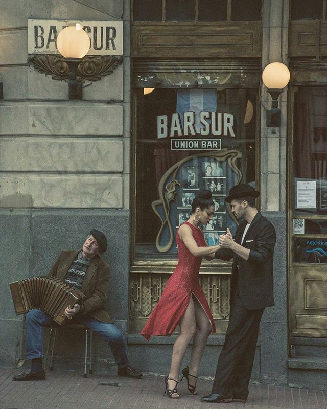 a man and woman standing in front of a bar with an accordion on the street