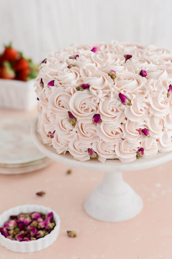 a cake with white frosting and pink flowers on top sitting on a table next to strawberries