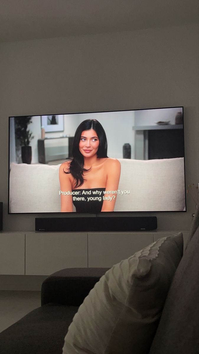 a flat screen tv mounted on the wall in a living room with couches and pillows