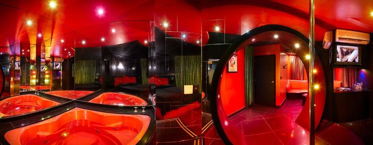 a red and black bathroom with two sinks in the middle, mirrors on the wall