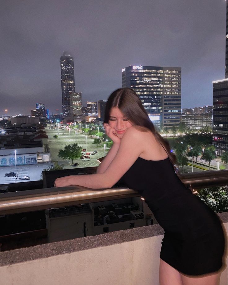 a woman leaning on a railing in front of a cityscape at night time