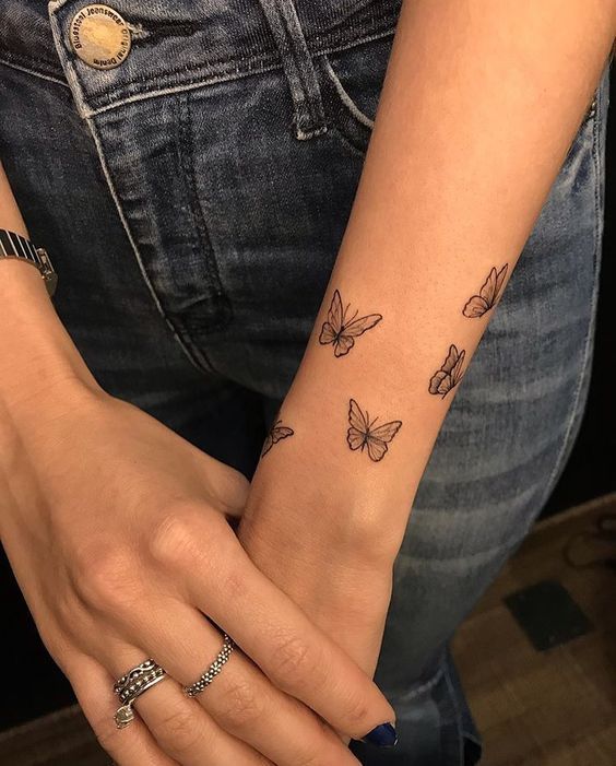 a woman's arm with butterfly tattoos on her left wrist and the other hand