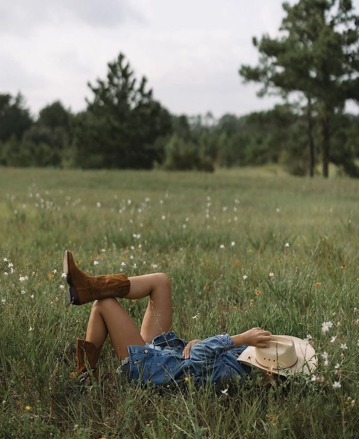 a woman laying on the ground in a field with her legs spread out and wearing cowboy boots