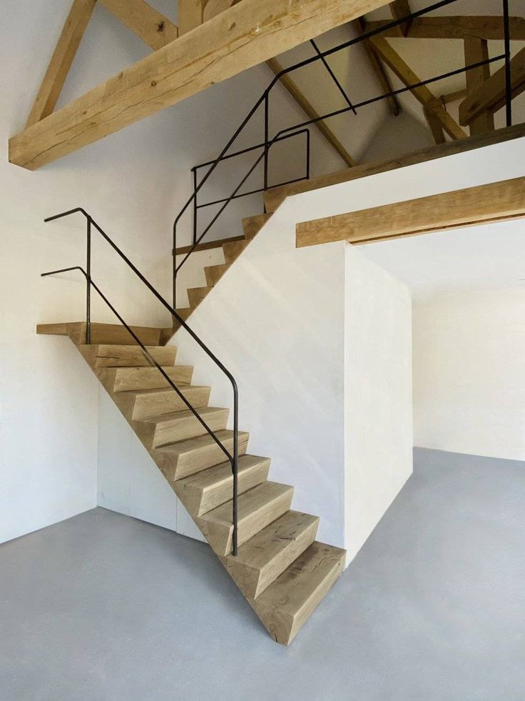 an empty room with some stairs and wooden beams on the ceiling, in front of a white wall