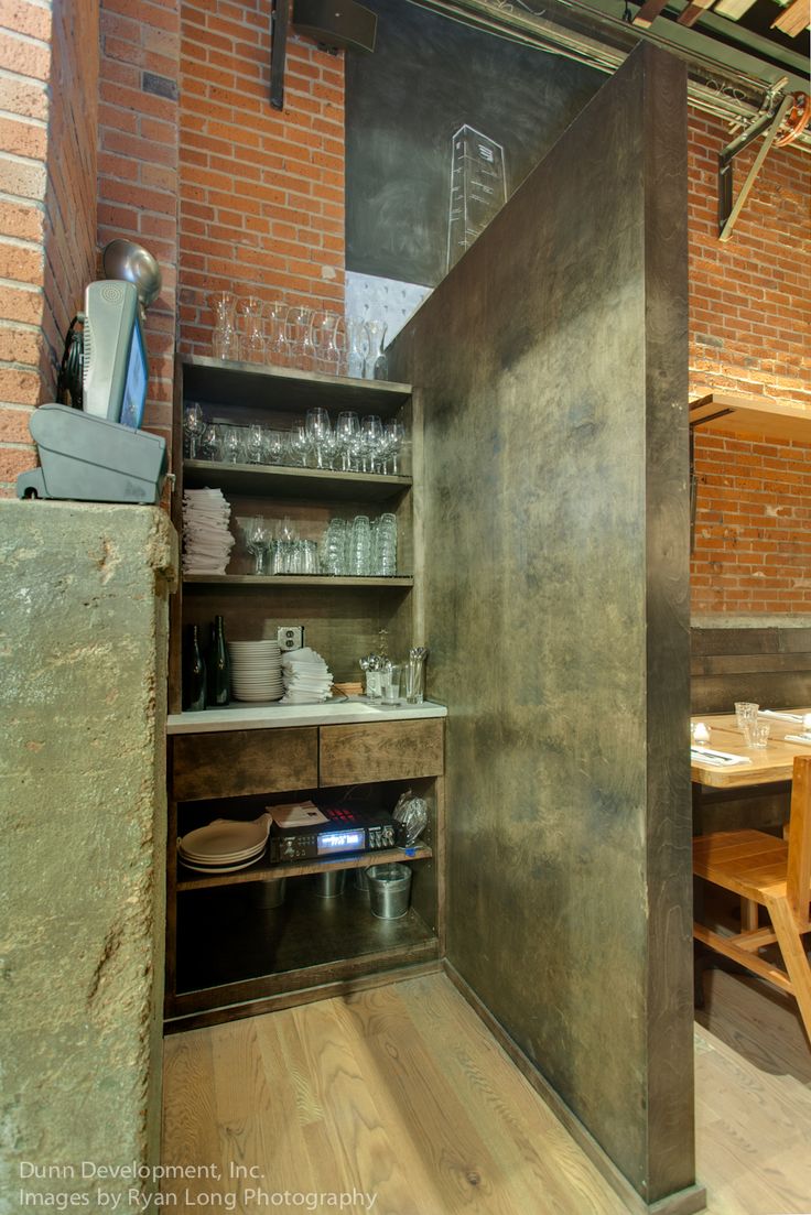 an open cabinet in the middle of a room with wooden tables and chairs around it