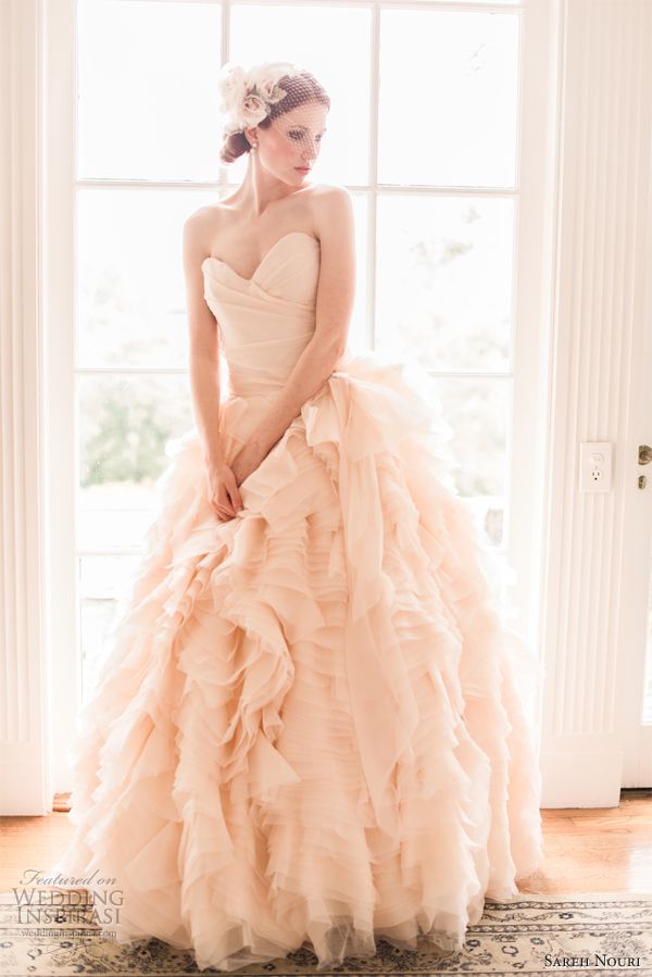 a woman in a wedding dress standing by a window with her hands on her hips