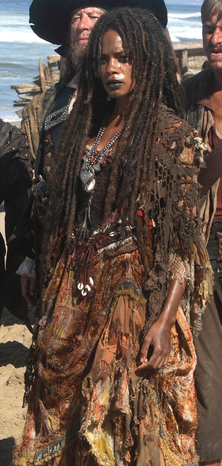 a woman with dreadlocks standing on the beach next to two men in pirate costumes