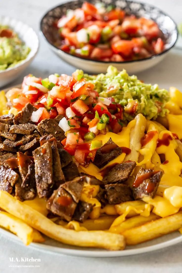 a plate filled with fries covered in cheese and toppings next to bowls of guacamole