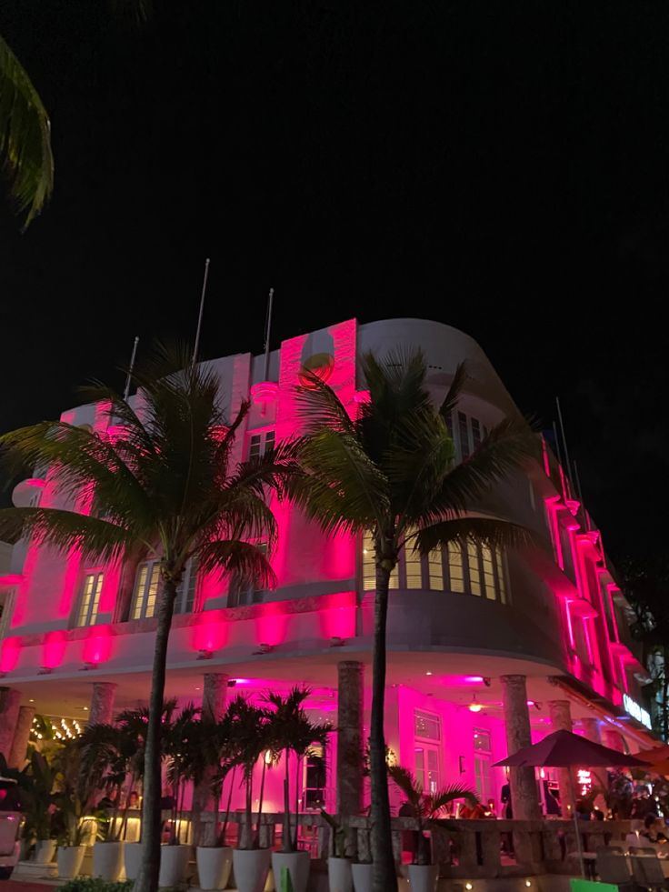 a large white building with pink lights on it's sides and palm trees in front