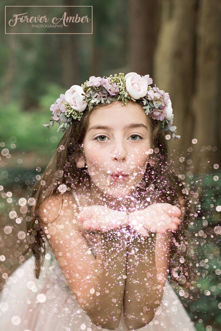 a woman in a white dress blowing bubbles with her hands and face covered by flowers