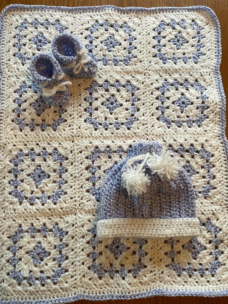 a crocheted baby blanket and hat on top of a wooden table next to a pair of shoes