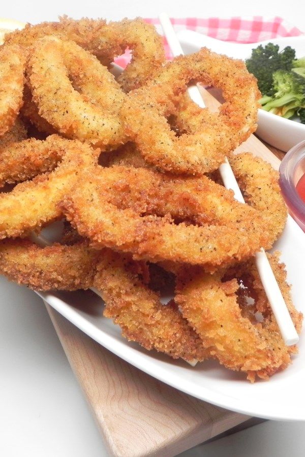 fried onion rings on a white plate with dipping sauce and broccoli in the background