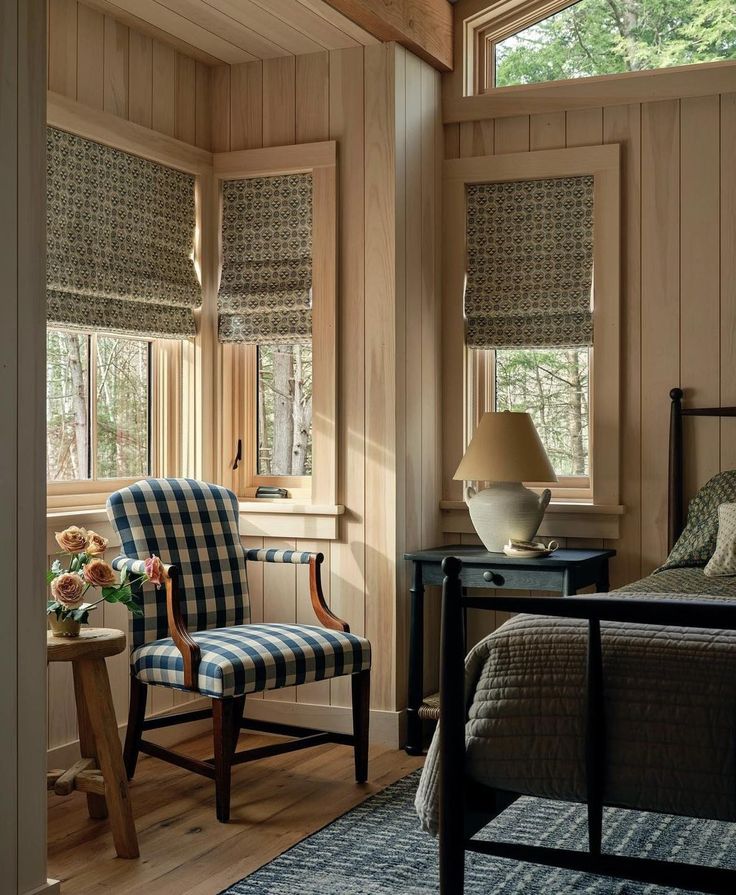 a bedroom with wood paneled walls and wooden furniture, along with two windows that have roman shades on them