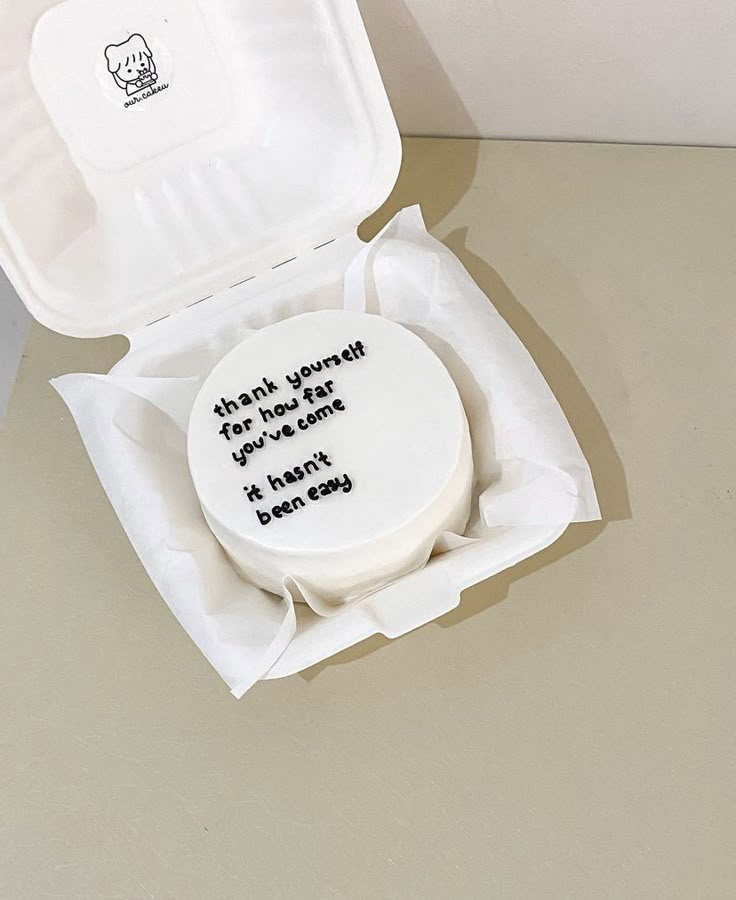 a white cake in a box with writing on the inside is sitting on a table