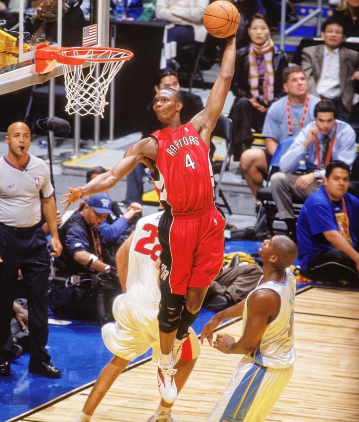 a basketball player dunks the ball in front of an opponent during a game with other players