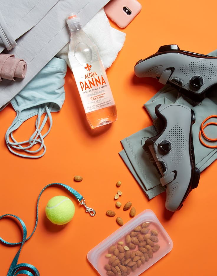 an assortment of sports equipment including shoes, water bottle and tennis ball on orange background