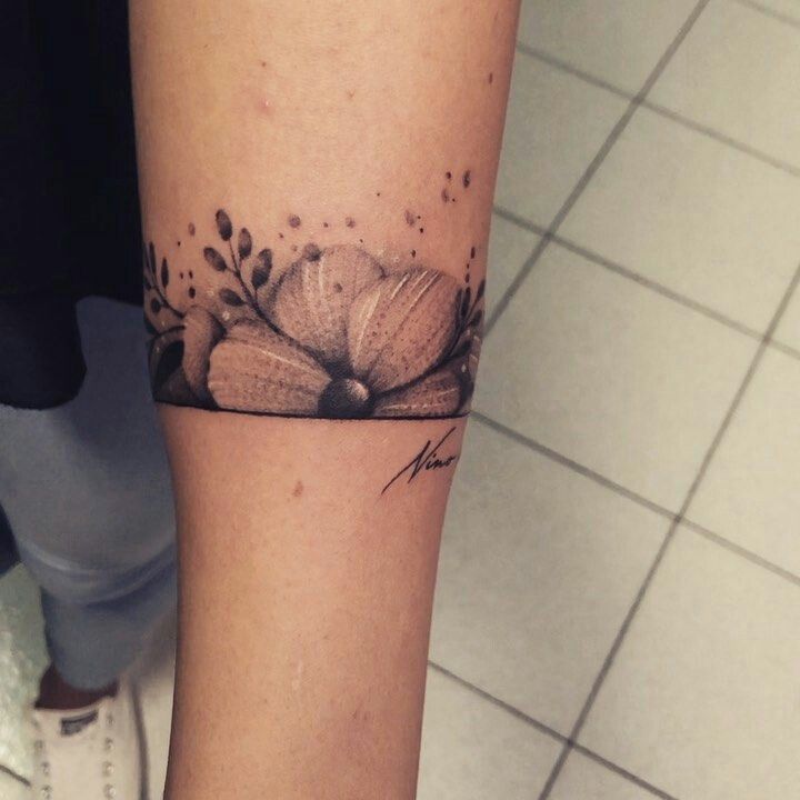 a woman's arm with a tattoo on it that has flowers and leaves around it