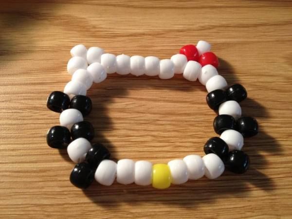 a close up of a bracelet made out of beads on a wooden table with a red, yellow and black bead