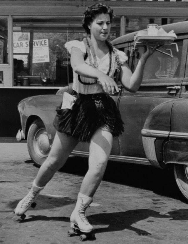 an old photo of a woman rollerblading in front of a car and holding a skateboard