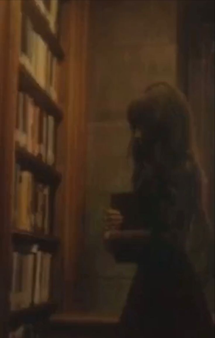 a woman standing in front of a bookshelf holding a cup and looking down