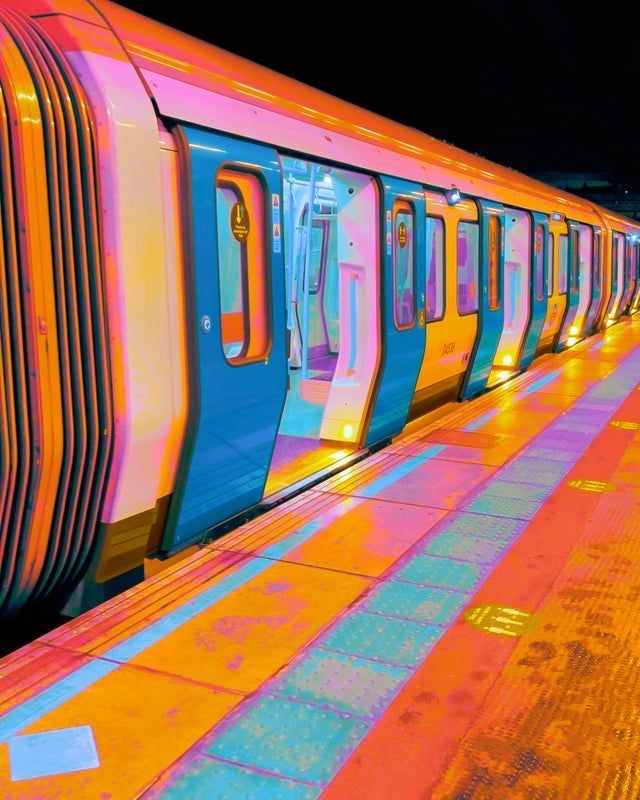 a colorful train stopped at a station with its doors open and lights on the side