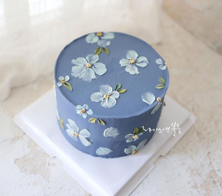 a blue cake with white flowers on it sitting on top of a counter next to a cell phone