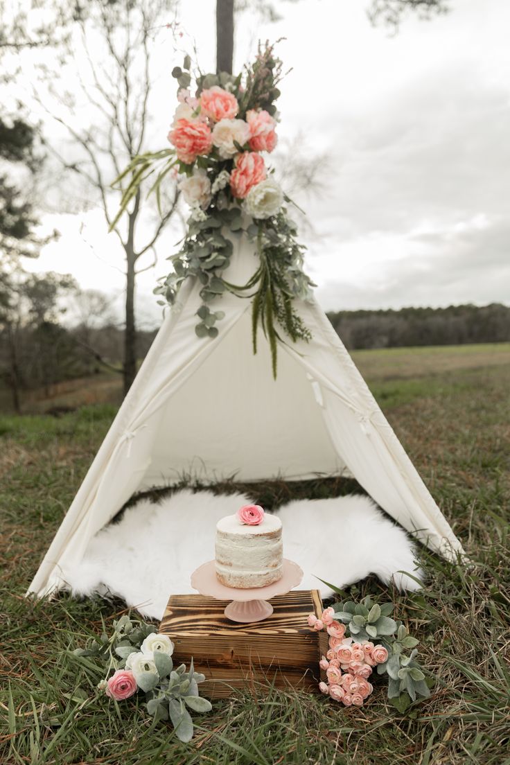 a cake sitting on top of a wooden box next to a teepee with flowers