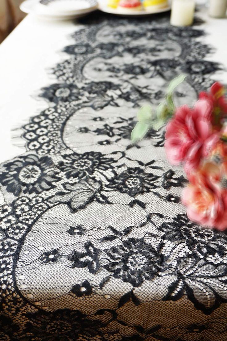 a table topped with a white and black lace covered table cloth next to a pink flower