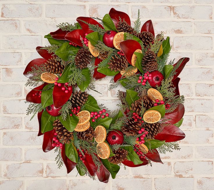 a christmas wreath with pine cones, poinsettis and berries on a brick wall