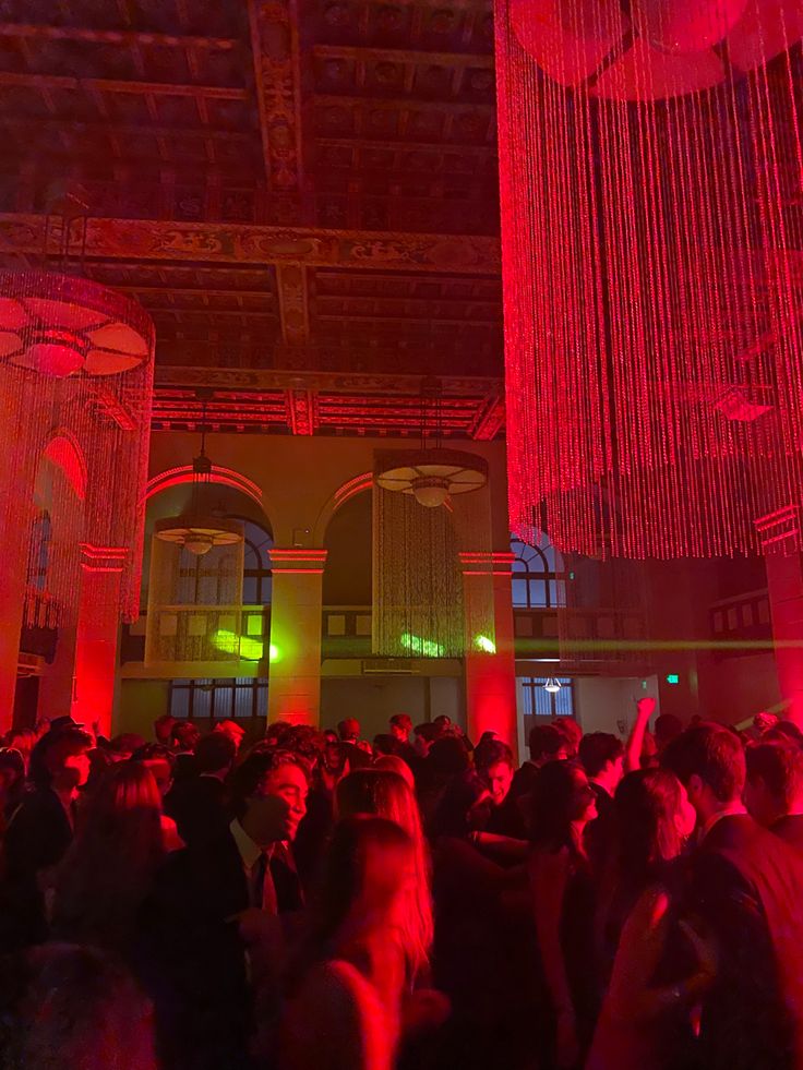 a large group of people in a room with red lights and chandeliers hanging from the ceiling