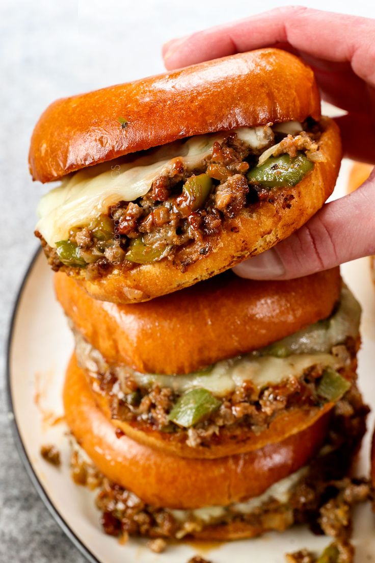 a hand holding a sandwich on top of a plate with other food items around it