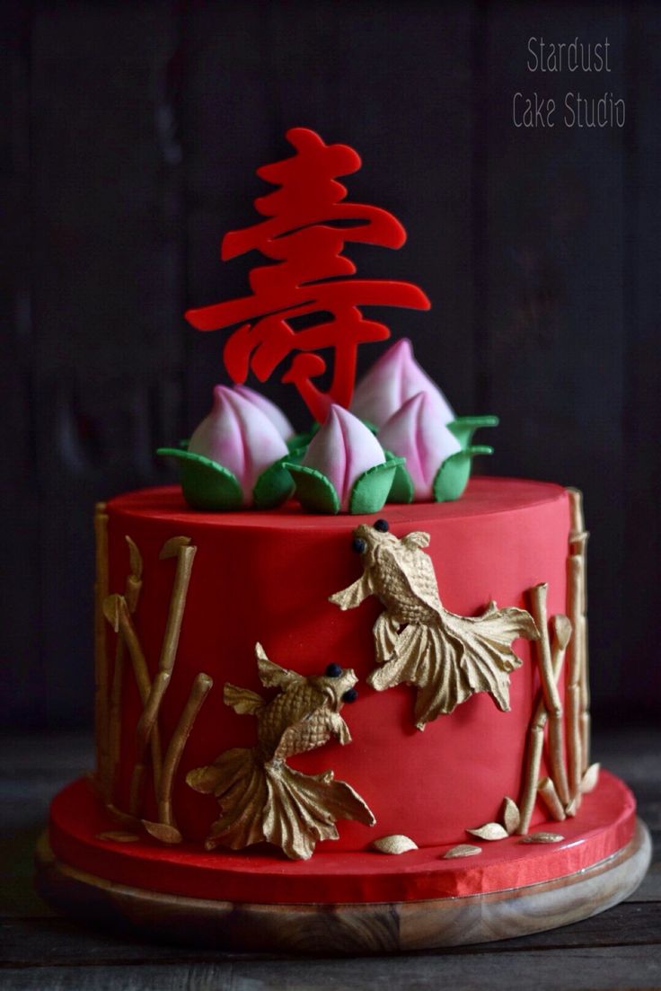 a red cake with gold decorations and flowers on the top is sitting on a wooden table