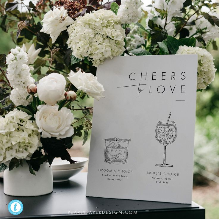 a table topped with white flowers next to a vase filled with greenery and wine glasses