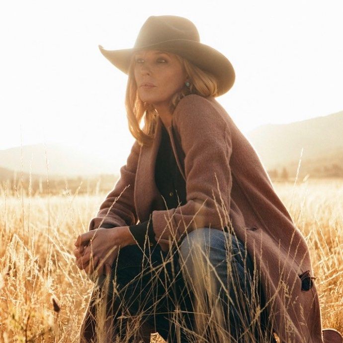 a woman wearing a cowboy hat sitting in the middle of a field with tall grass