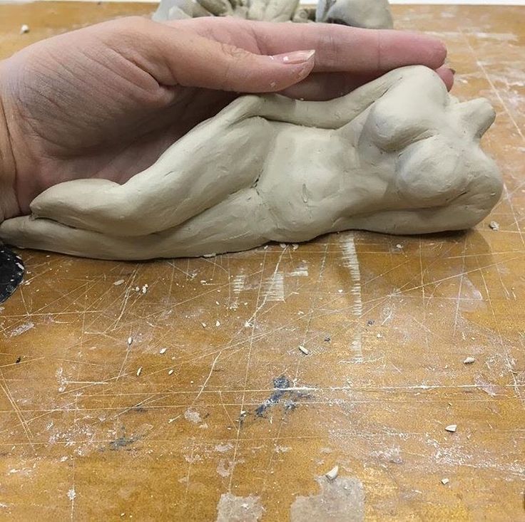 a hand holding a clay animal on top of a wooden table next to a piece of wood