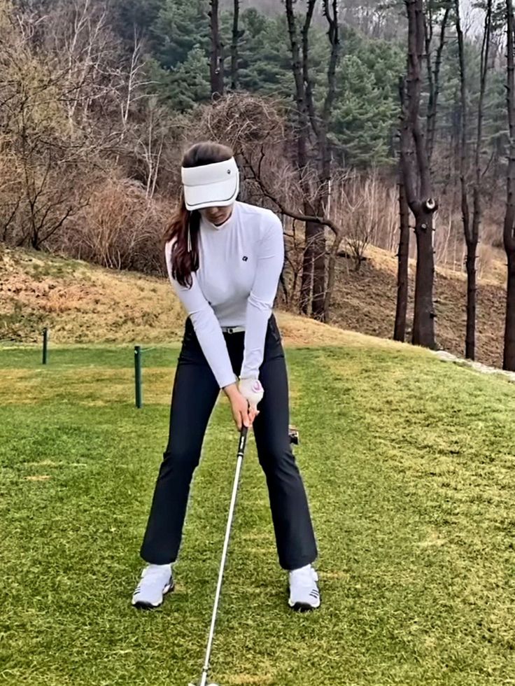 a woman wearing a blindfold playing golf on the green with trees in the background