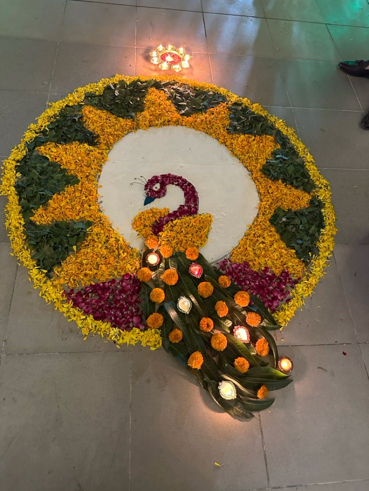 a peacock made out of flowers and lit candles on the ground in front of it