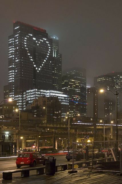 the city skyline is lit up at night, with buildings in the foreground and cars on the road