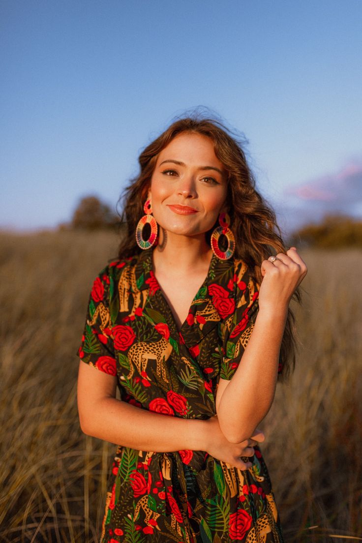 a woman standing in a field with her hands on her hips and wearing large earrings