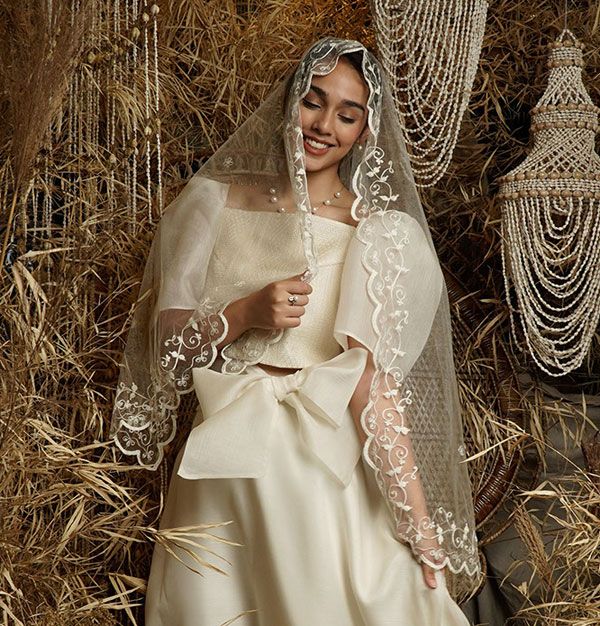 a woman in a wedding dress standing next to a pile of hay and wearing a veil