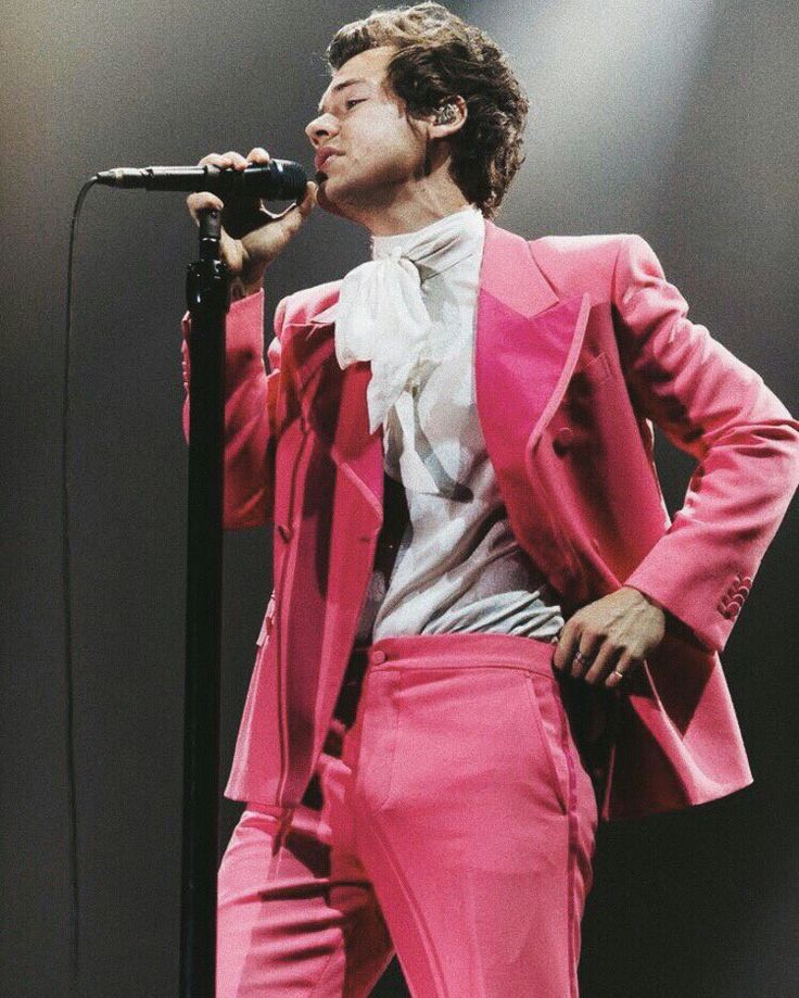 a male in a pink suit and white shirt singing into a microphone while standing on stage