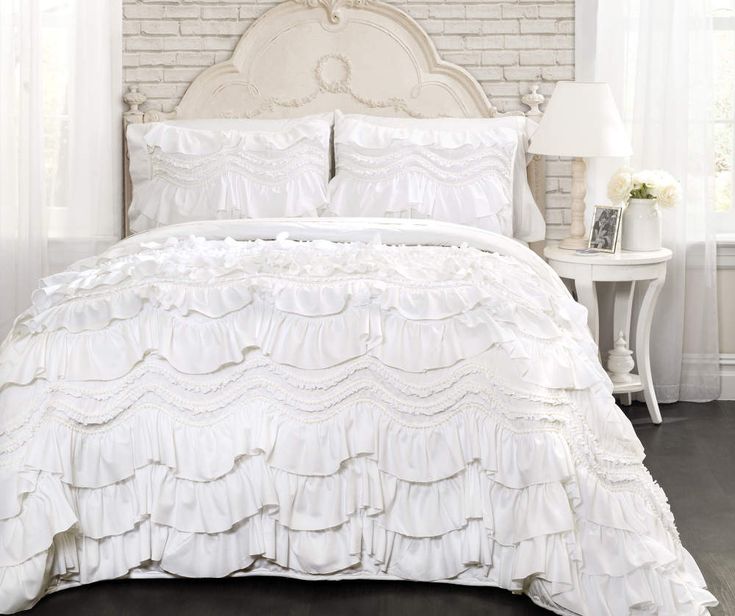 a white bed with ruffled bedspread and pillows