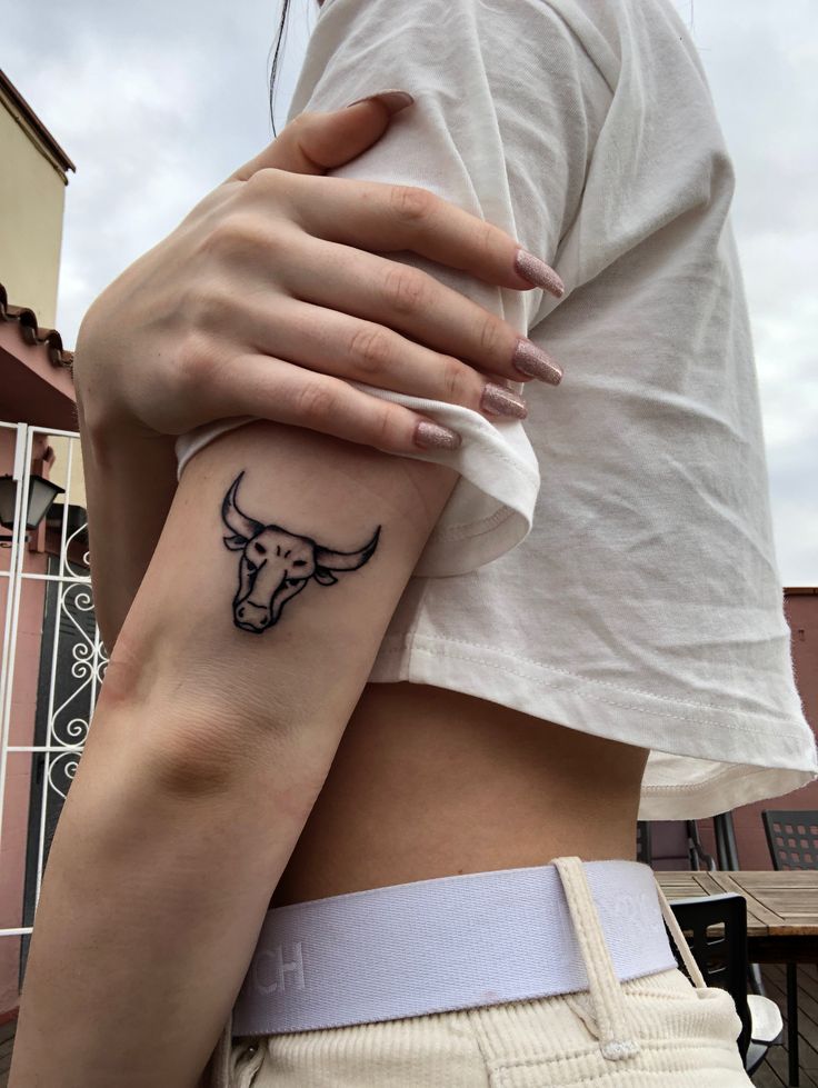 a woman with a bull tattoo on her left arm and the other arm behind her