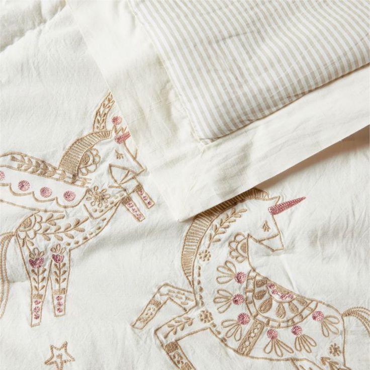 an embroidered bed spread with two horses on it's side and a striped pillow case in the background