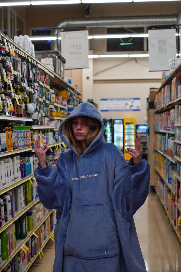 a woman in a blue hoodie is walking through a store aisle with her hands up