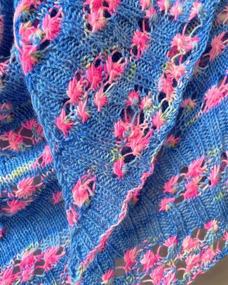 a crocheted blue blanket with pink flowers on it